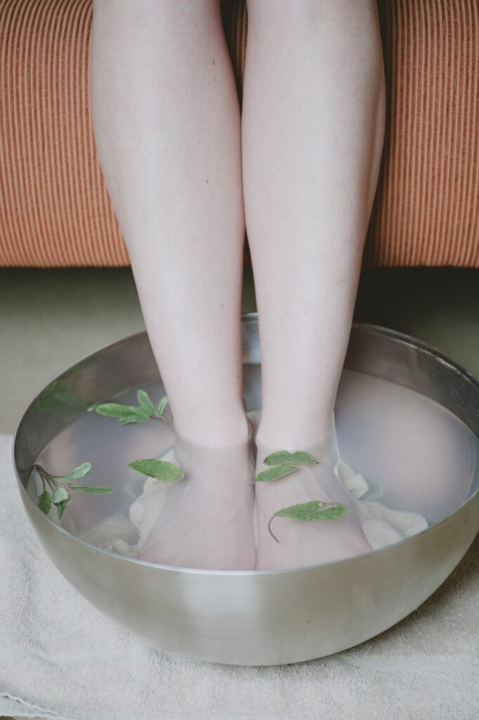Woman soaking feet in epsom salt and water with herbs.