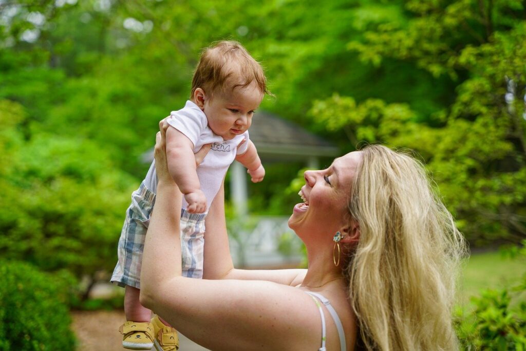 Mother holding infant and smiling outside. 