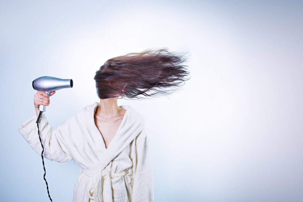 Woman blow drying hair sideways.