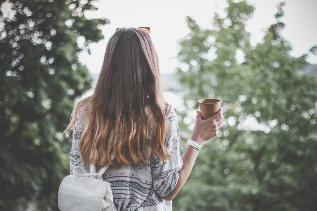 Woman standing with back to camera with coffee in hand and long hair. 